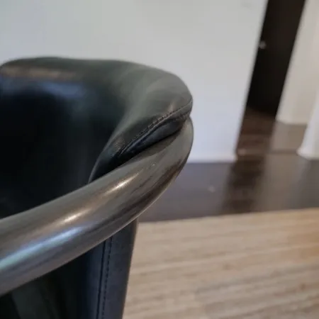 Close-up of a black leather chair armrest with a smooth metal frame in a modern room.