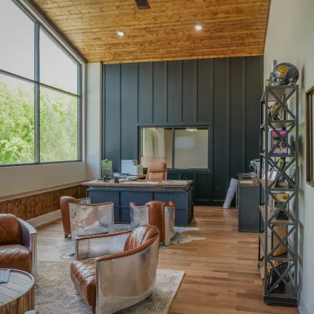Modern office space with large windows, leather chairs, wooden floors, and a black accent wall.