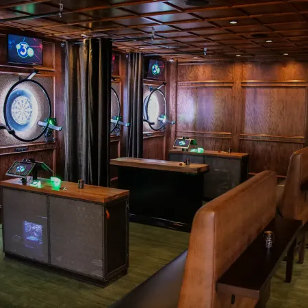 Modern indoor dart area with electronic dartboards, wooden counters, and leather booth seating under warm lighting.