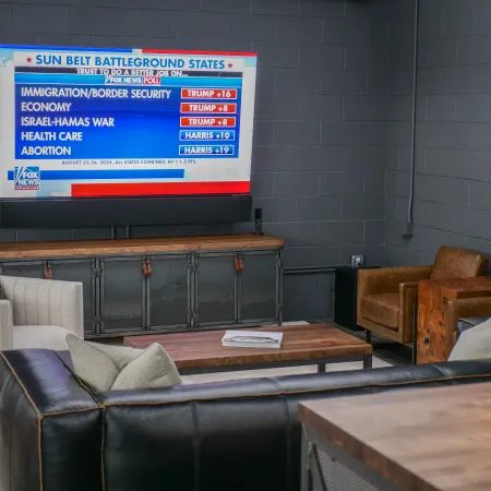 Living room with modern leather and fabric furniture and a TV showing Fox News poll on battleground states' trust in candidates.