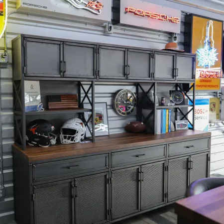 Industrial-style metal cabinet with sports helmets, books, clock, and Porsche neon signs on garage wall
