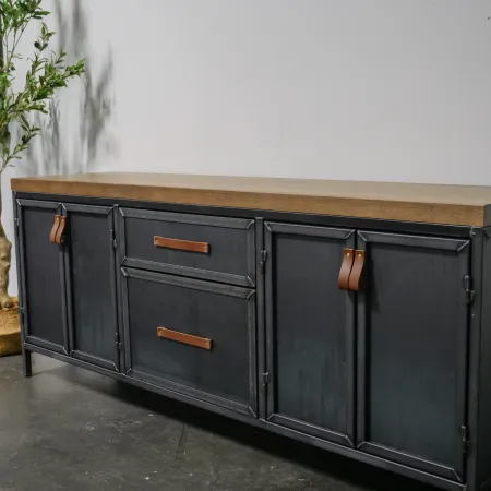 Industrial style black metal sideboard with wooden top and leather handles, next to a potted tree indoors.