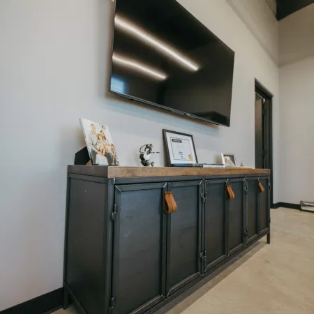 Modern black metal sideboard with leather handles under a large flat screen TV mounted on white wall.
