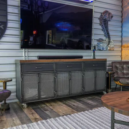 Modern automotive-themed lounge with leather chairs, TV, wooden table, and vintage car wall art.