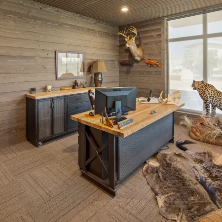 Modern rustic office with wooden walls, animal mountings, a wooden desk, and a leopard decor by large windows