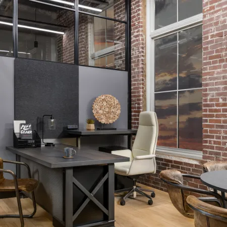 Modern office with wooden floors, exposed brick walls, large windows, stylish chairs, and contemporary desk setup.
