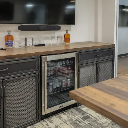 Modern office area with a wooden countertop, metal cabinets, mini fridge stocked with cans, and mounted TV.