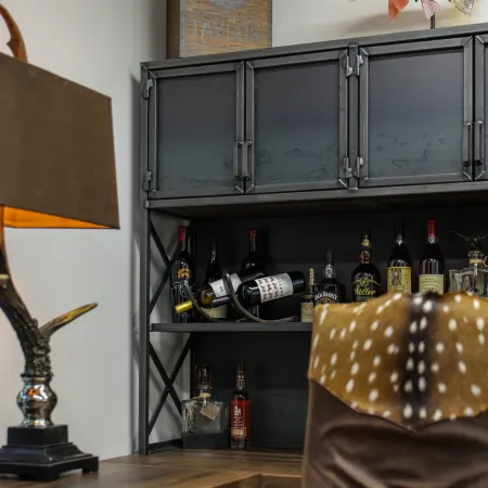 Stylish brown and beige lamp beside a bar cabinet filled with various liquor bottles in a cozy room.