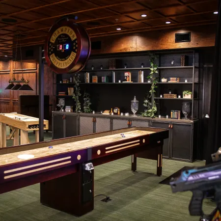 Indoor game room with shuffleboard tables, dartboard, wooden shelves, and cozy lighting in a recreational space