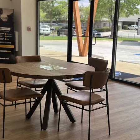 Round wooden table with four brown chairs in a room with large glass windows and wood flooring.