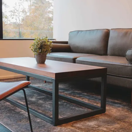 Modern living room with a gray sofa, wooden coffee table, leather chair, and large window with autumn view.
