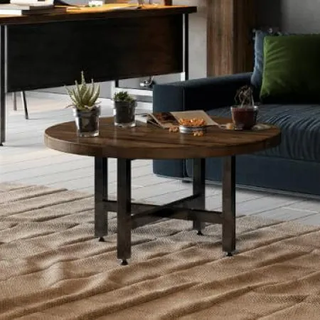 Round wooden coffee table with plants and snacks in a modern living room with dark blue couch and desk.
