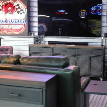 Modern gaming room with a large TV, leather sofa, neon sign, and automotive-themed decor.