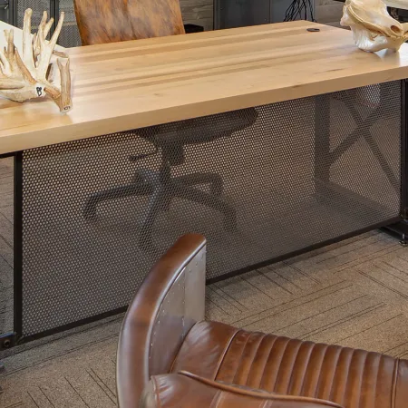 Modern office desk with wooden top, metal frame, leather chair, and decorative animal skulls on a carpeted floor.