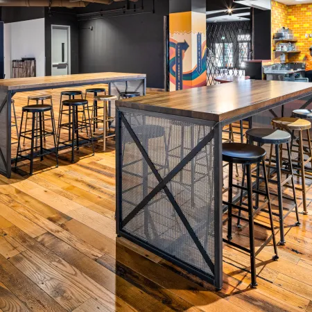 Modern café interior with high wooden tables, metal stools, colorful wall art, and warm hardwood flooring.