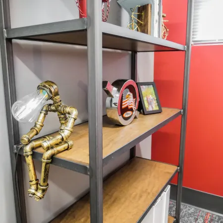 Industrial-style metal and wood shelving with a pipe lamp figure, clock, and photo frame against red wall.