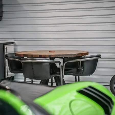 Modern garage with round wooden table, black chairs, green car hood, and storage cabinets