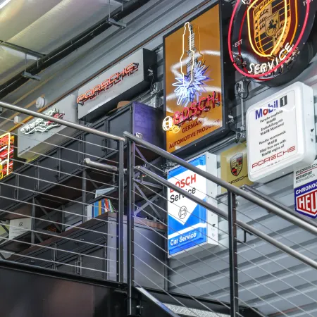 Interior of a modern showroom wall decorated with illuminated Porsche and automotive service signs.