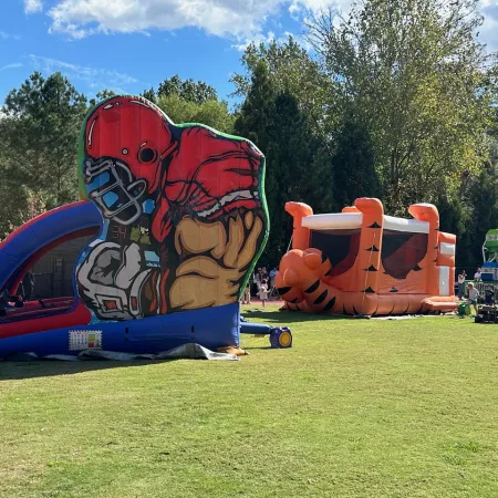 Colorful inflatable football player and tiger bounce houses set up on grass during a sunny outdoor event.