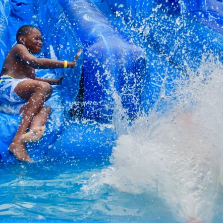 Boy enjoying a blue inflatable water slide splashing into the pool on a sunny day.