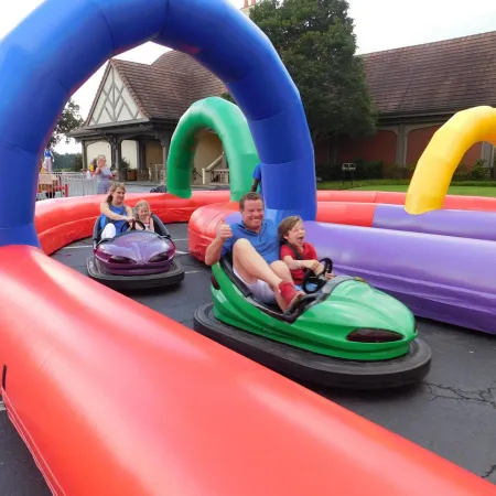 Kids and adults enjoying colorful inflatable bumper car ride outdoors with arches and cheerful expressions