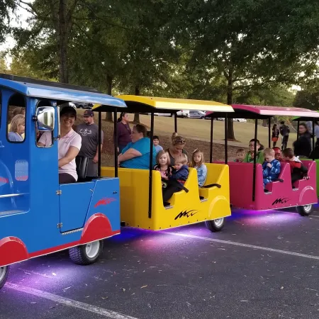 Colorful outdoor train ride with children and adults enjoying evening in park, with purple underglow lights