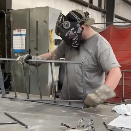 Man wearing protective helmet and gloves assembling metal frame in industrial workshop.