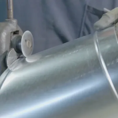 Worker wearing gloves cutting metal sheet using a grinding tool in a workshop environment.