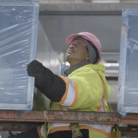 Construction worker in safety gear handling large insulated panels inside an industrial building environment.