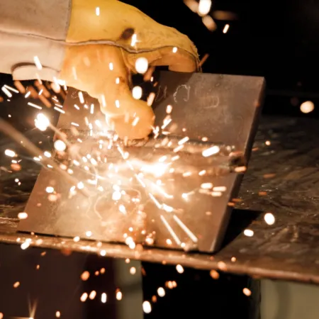 Close-up of welding sparks flying from metal being worked on by gloved hands in industrial setting