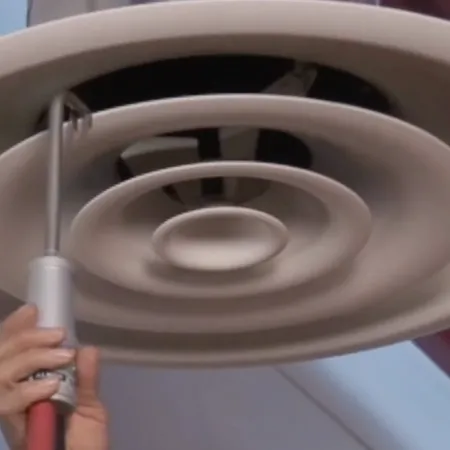 Hand adjusting circular ceiling air vent with a red-handled tool in an indoor setting.