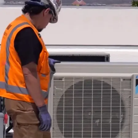 Technician in safety gear inspects Daikin air conditioning units on a rooftop with a fire hydrant in view.