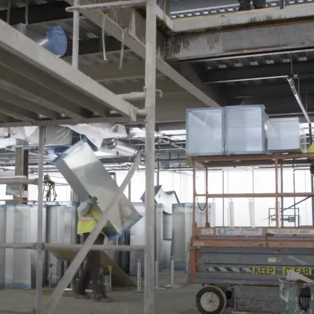Construction workers installing HVAC ductwork inside a commercial building under construction with scaffolding and equipment.