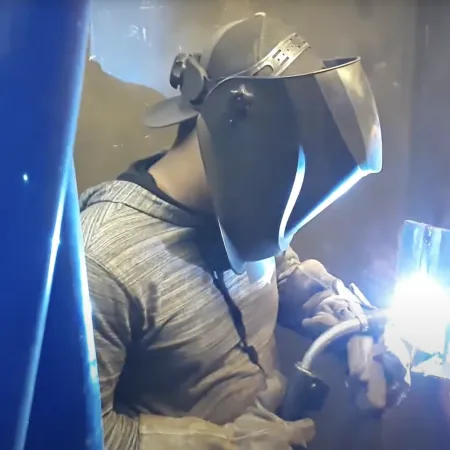 Man wearing protective welding helmet and gloves working with bright welding torch indoors