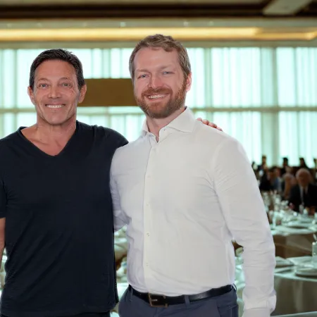 Two men smiling and posing together at a formal banquet setting with tables and guests in the background