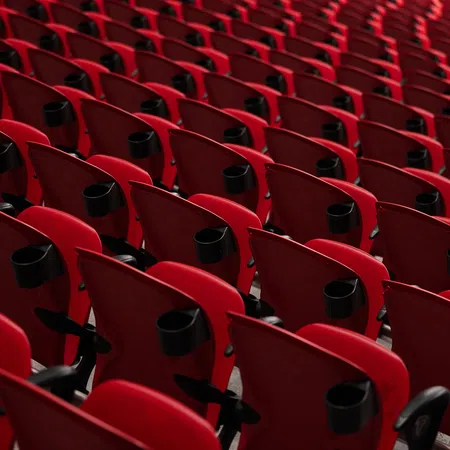 Rows of empty red stadium seats with black cup holders arranged in a pattern under soft lighting.