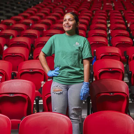 Woman in green shirt and blue gloves standing confidently among empty red stadium seats