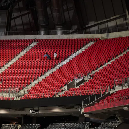 Empty red stadium seats with two workers performing maintenance in the middle section under industrial ceiling.