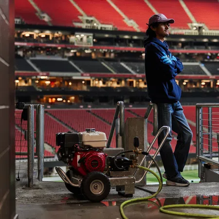Man in casual clothing stands next to industrial equipment inside an empty sports stadium tunnel.