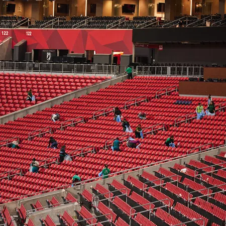 Workers cleaning and disinfecting rows of empty red stadium seats before an event starts.