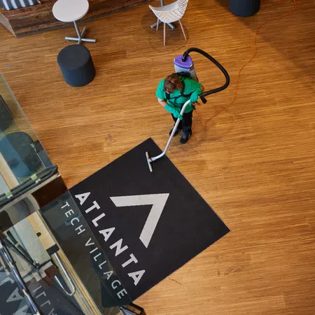 Person cleaning a black Atlanta Tech Village floor mat on wooden floor in modern office lobby