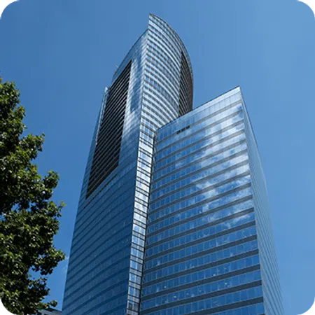 Modern glass skyscraper reflecting blue sky and clouds with green tree on the side