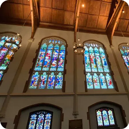 Interior view of a church with large stained glass windows and wooden vaulted ceiling with chandeliers.