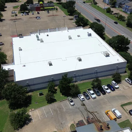 Aerial view of a completed white TPO membrane roof on a large commercial retail building in College Station, Texas, showing the full flat roof system with rooftop HVAC units and parking areas surrounding the property.