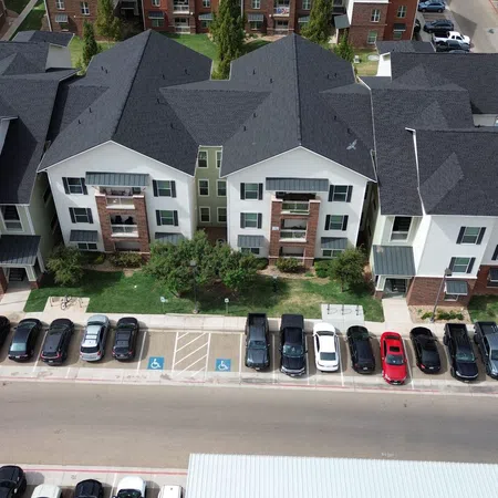 Newly reroofed three-story multi-family townhome building in Lubbock, Texas with charcoal architectural shingles, white siding, and brick lower level, completed by Mattco Roofing and Construction.