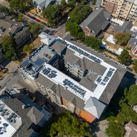 Aerial view of a student housing TPO reroof in Austin, Texas, with new white membrane roofing installed around rooftop HVAC equipment, patio decks, and a central courtyard on a multi-story residential building near the University of Texas campus.
