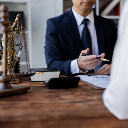 Lawyer in navy suit discussing a legal document with client at wooden desk with scales of justice.