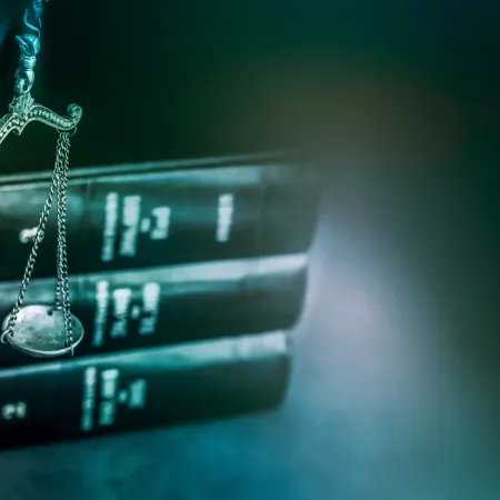 Close-up of Lady Justice statue with scales and legal books in the background on blue gradient.
