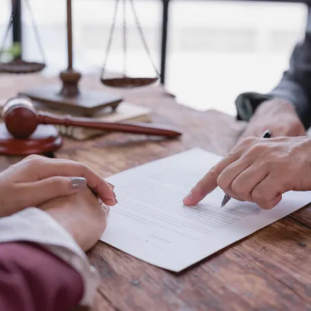 Lawyer pointing to a document while client listens at a wooden desk with legal scales and gavel