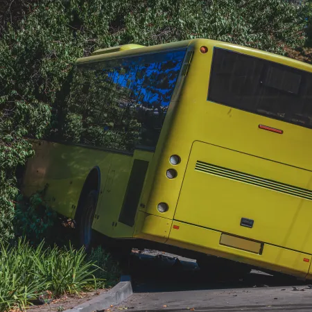 Yellow bus partially off the road near trees and a traffic cone on a sunny day.